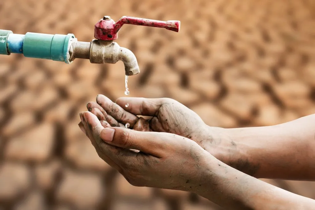 dirty-hand-wating-water-drop-from-faucet-with-dry-cracked-earth-backgroung