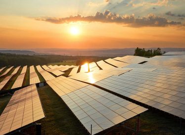 Placas solares en el campo con el cielo atardeciendo y el sol incidiendo sobre ellas